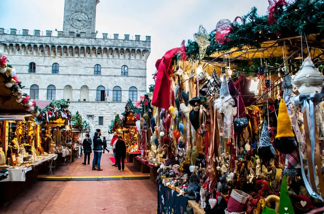 Mercatino di Natale a Montepulciano con bancarelle piene di decorazioni e gente che passeggia.