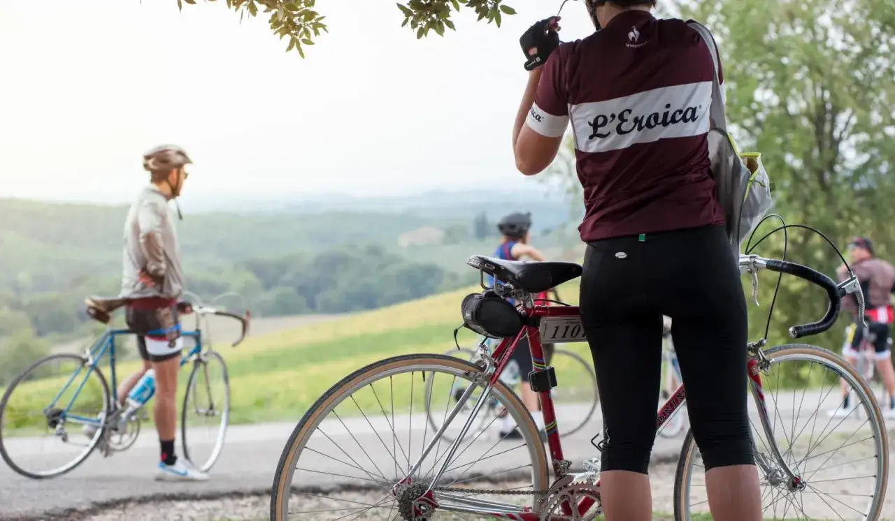 Ciclisti con bici d'epoca su una strada eroica toscana, con paesaggio collinare sullo sfondo.