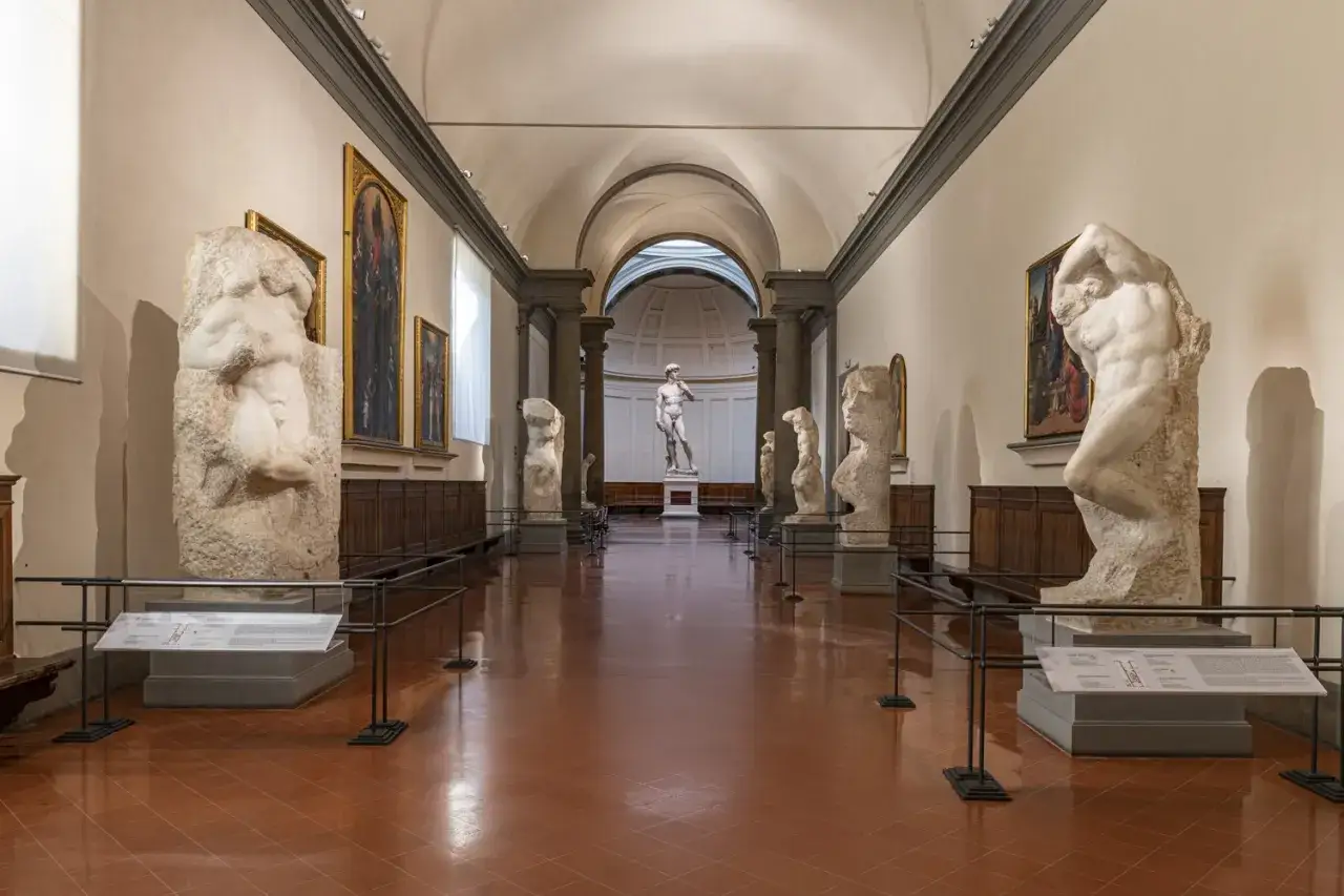 Corridoio dei musei d'arte a Firenze con sculture rinascimentali, tra cui il David di Michelangelo in fondo.