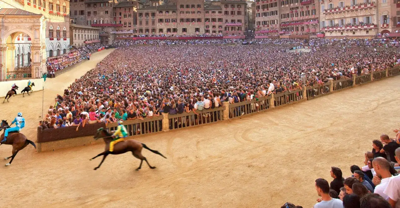 Cavalli e fantini corrono nella piazza gremita di spettatori. Si percepisce l'emozione di quand'è il Palio di Siena.