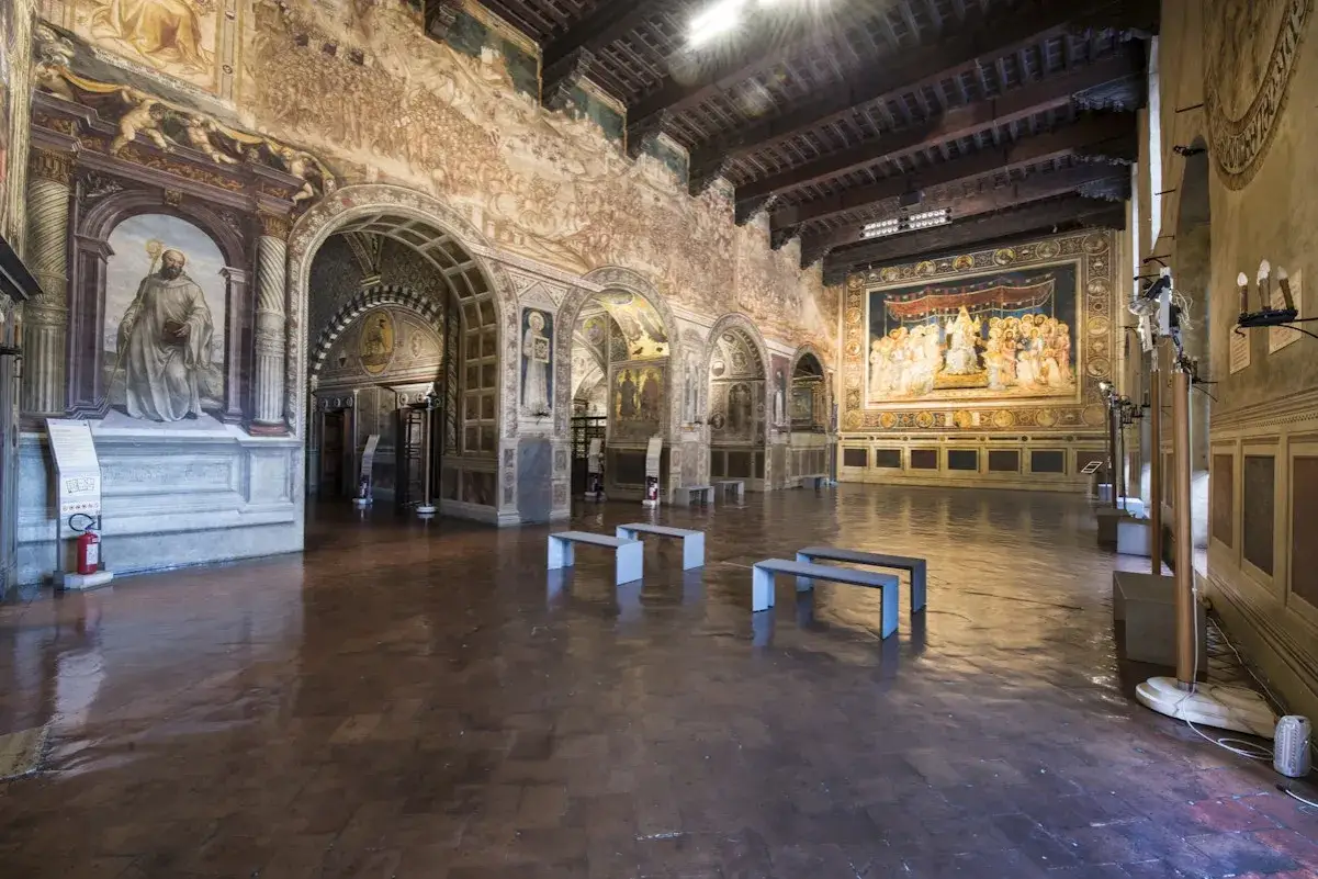 Interno di un museo a Siena con affreschi storici e panche moderne.