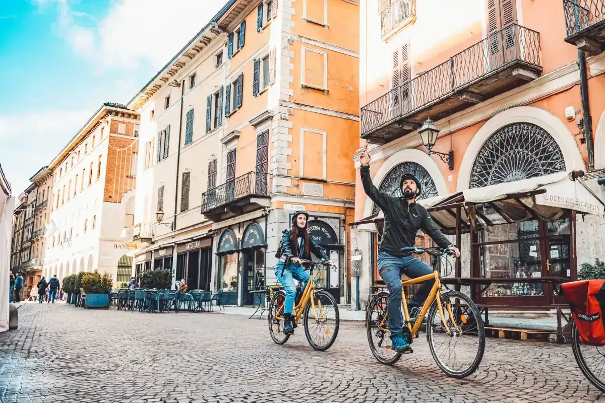 Coppia in bici esplora una citt&agrave; storica, perfetta per itinerari bici 3 giorni. Edifici colorati e ciottoli creano un'atmosfera suggestiva.