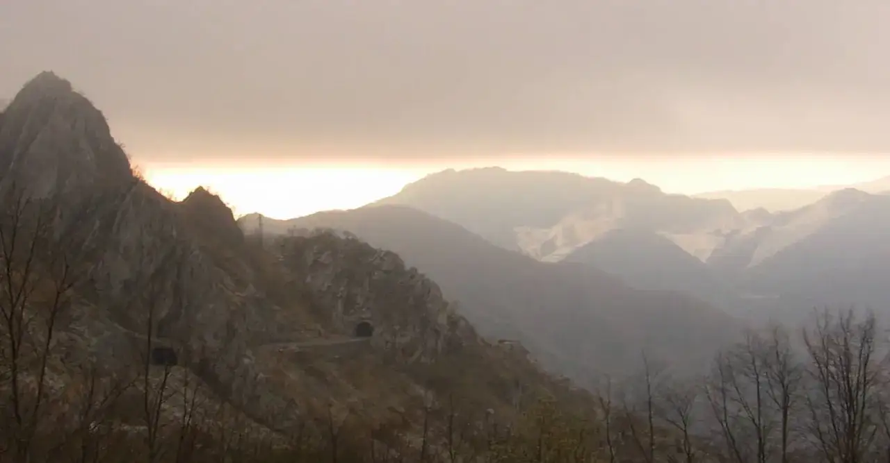 Paesaggio montano con un tunnel scavato nella roccia, che sembra l'apertura di un passo del vestito. La luce del tramonto illumina le cime.