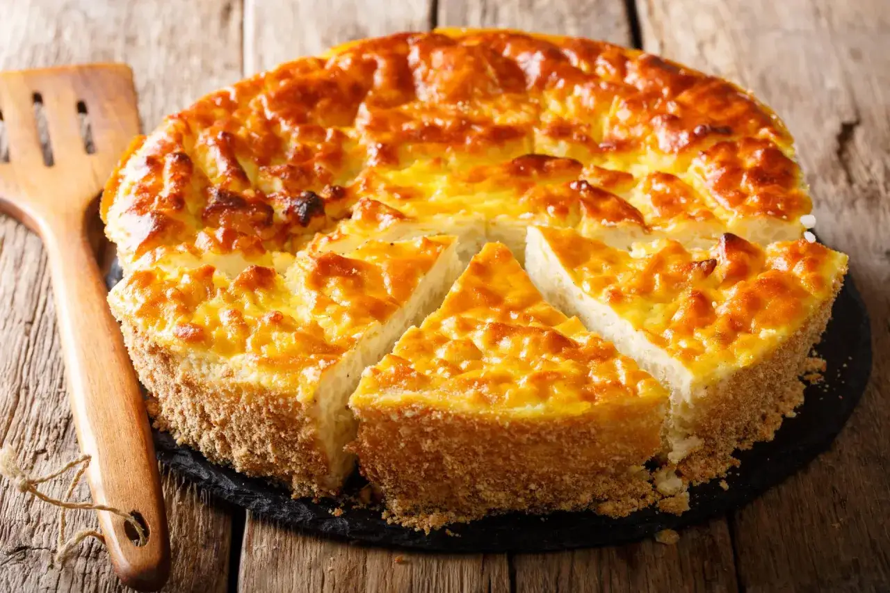 Torta soffice e dorata, uno dei classici dolci emiliani, pronta per essere gustata. Accanto, una spatola in legno.