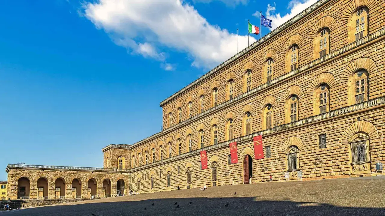 Il maestoso Palazzo Pitti a Firenze, con la sua imponente facciata in bugnato, si staglia sotto un cielo azzurro con nuvole bianche.