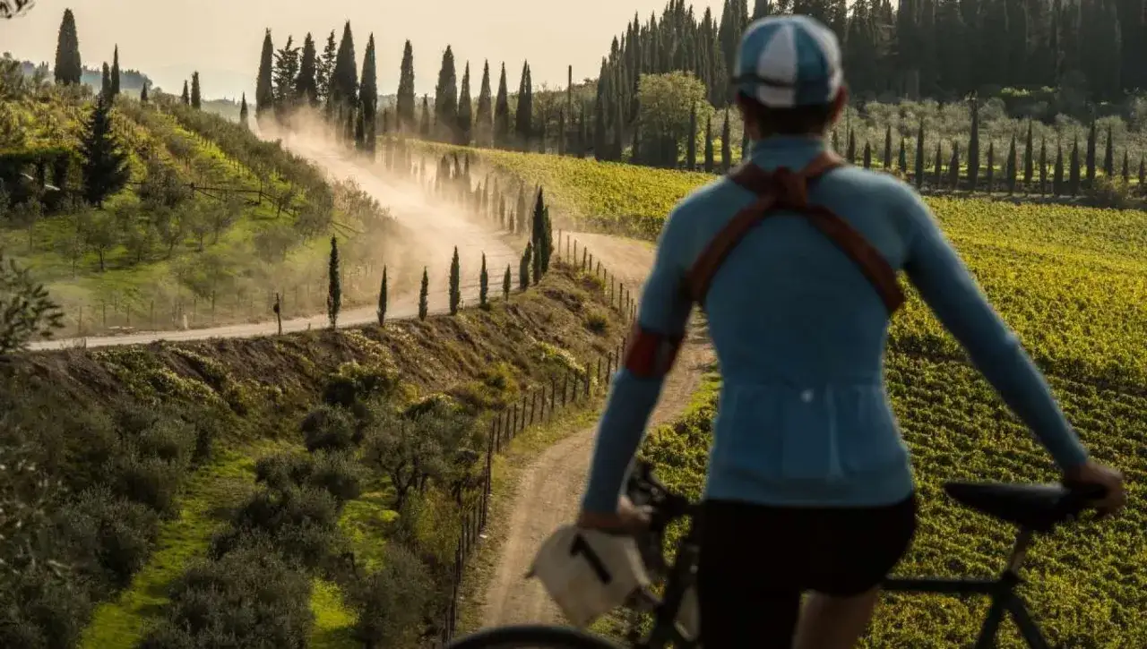 Ciclista su strada sterrata in Toscana, tra vigneti e ulivi. Un eroico percorso che solleva polvere sotto il sole.