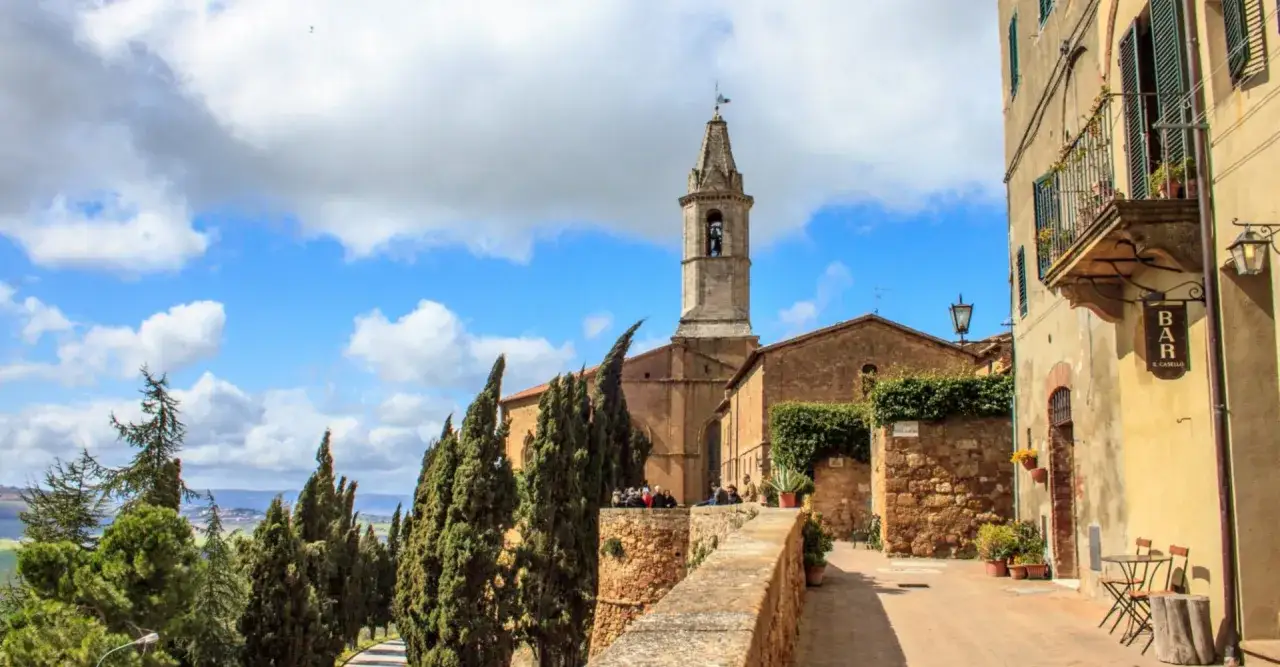 Un borgo toscano con un campanile svetta su un paesaggio collinare. Perfetto per un itinerario Val d'Orcia 3 giorni.