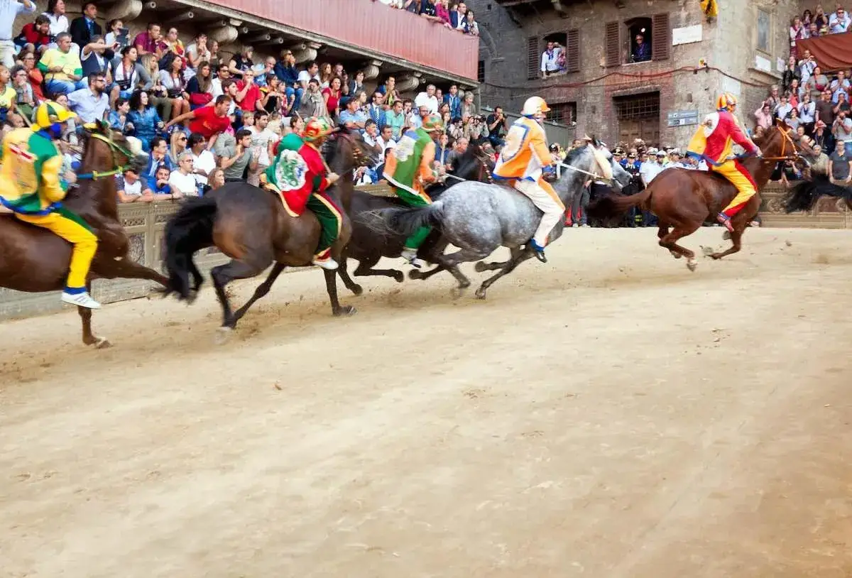 Cavalli e fantini in corsa, un'emozionante dimostrazione di come si celebra il Palio di Siena, con la folla che assiste.