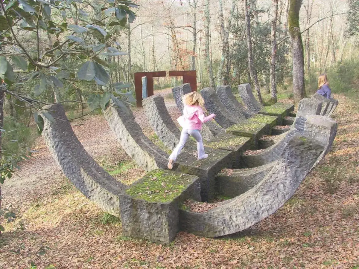 Bambini esplorano un museo a cielo aperto in Toscana, tra sculture in pietra e alberi secolari.