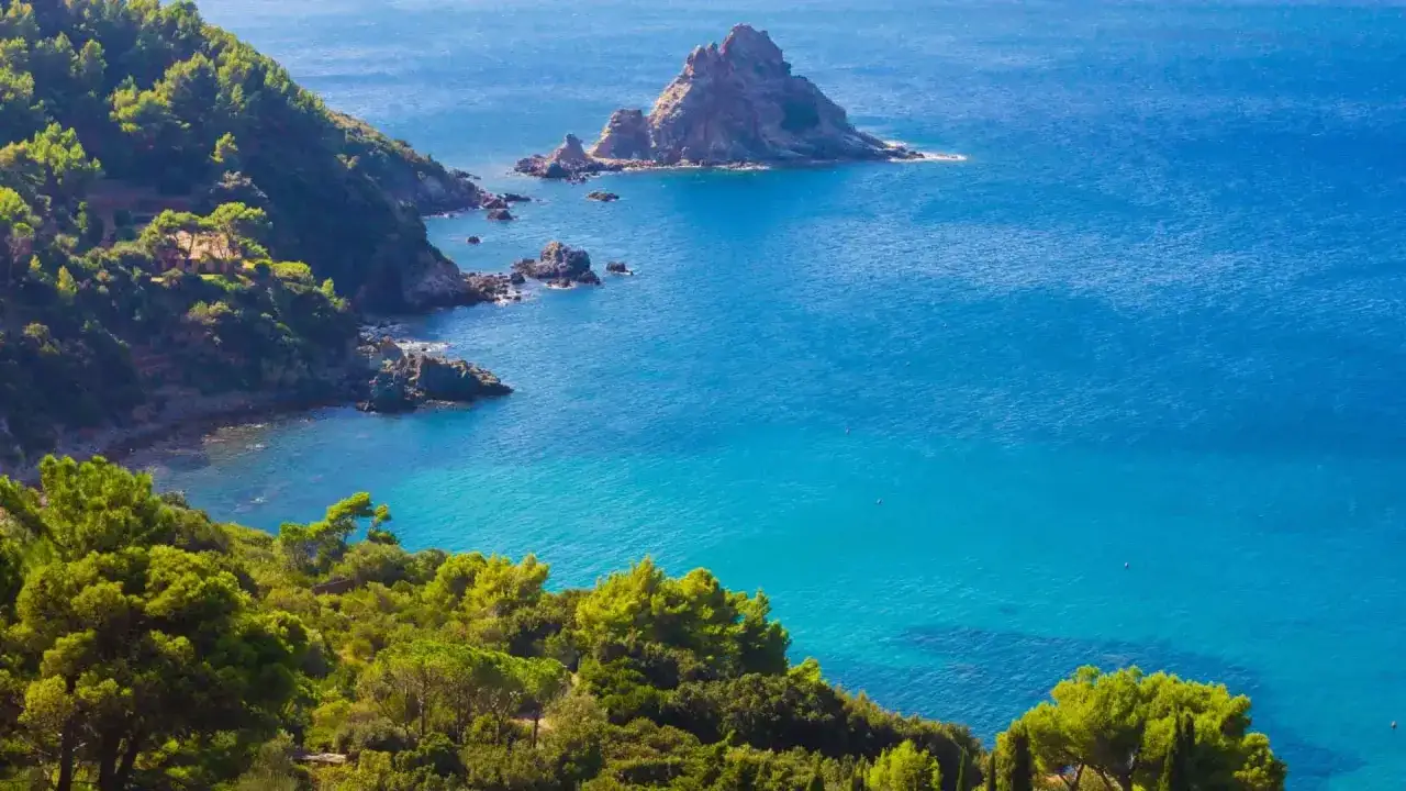 Scogliera verdeggiante e mare azzurro intenso vicino al Monte Argentario, con un faraglione solitario.