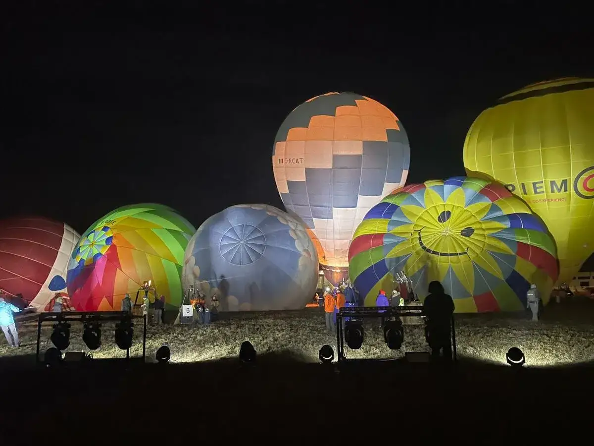 Un evento mongolfiere notturno con palloni colorati, tra cui uno con un grande sorriso, pronti al decollo.