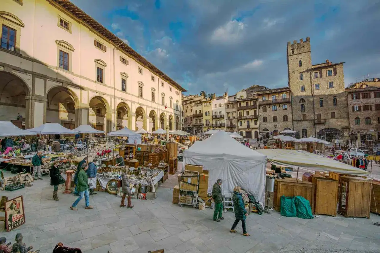 Mercato all'aperto a San Gimignano, con bancarelle piene di oggetti d'antiquariato e persone che passeggiano tra le tende bianche.