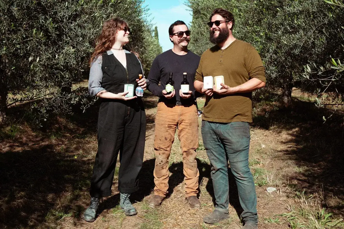 Tre amici celebrano la festa dell'olio tra gli ulivi, tenendo bottiglie e confezioni.