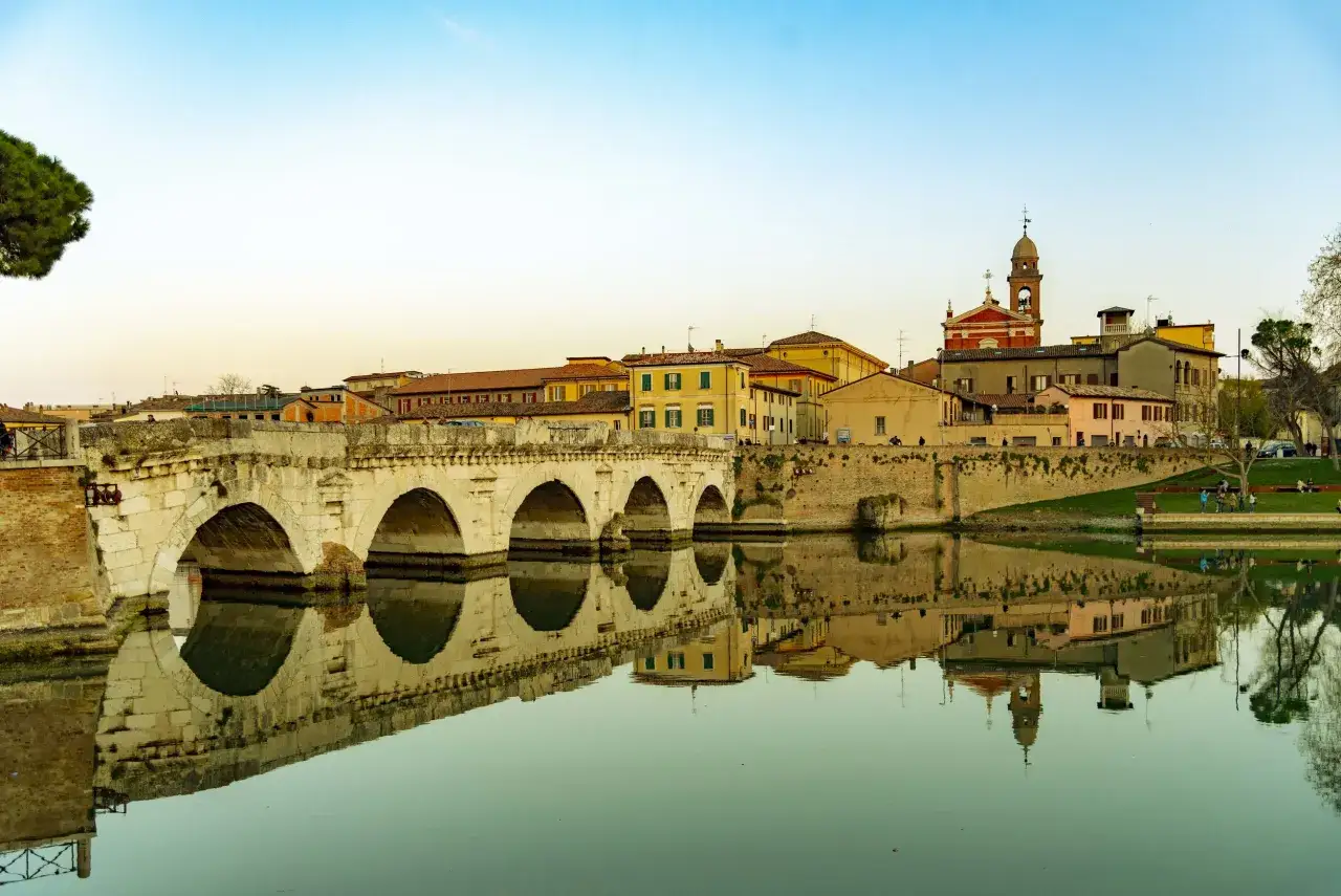 Ponte di Tiberio e il borgo antico, un'immagine iconica di cosa vedere a Rimini, con riflessi sull'acqua calma.