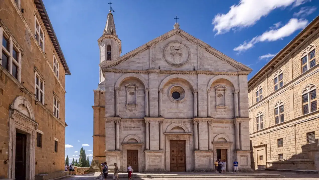 La piazza di Pienza, con la sua imponente cattedrale e palazzi rinascimentali, accoglie visitatori sotto un cielo azzurro.