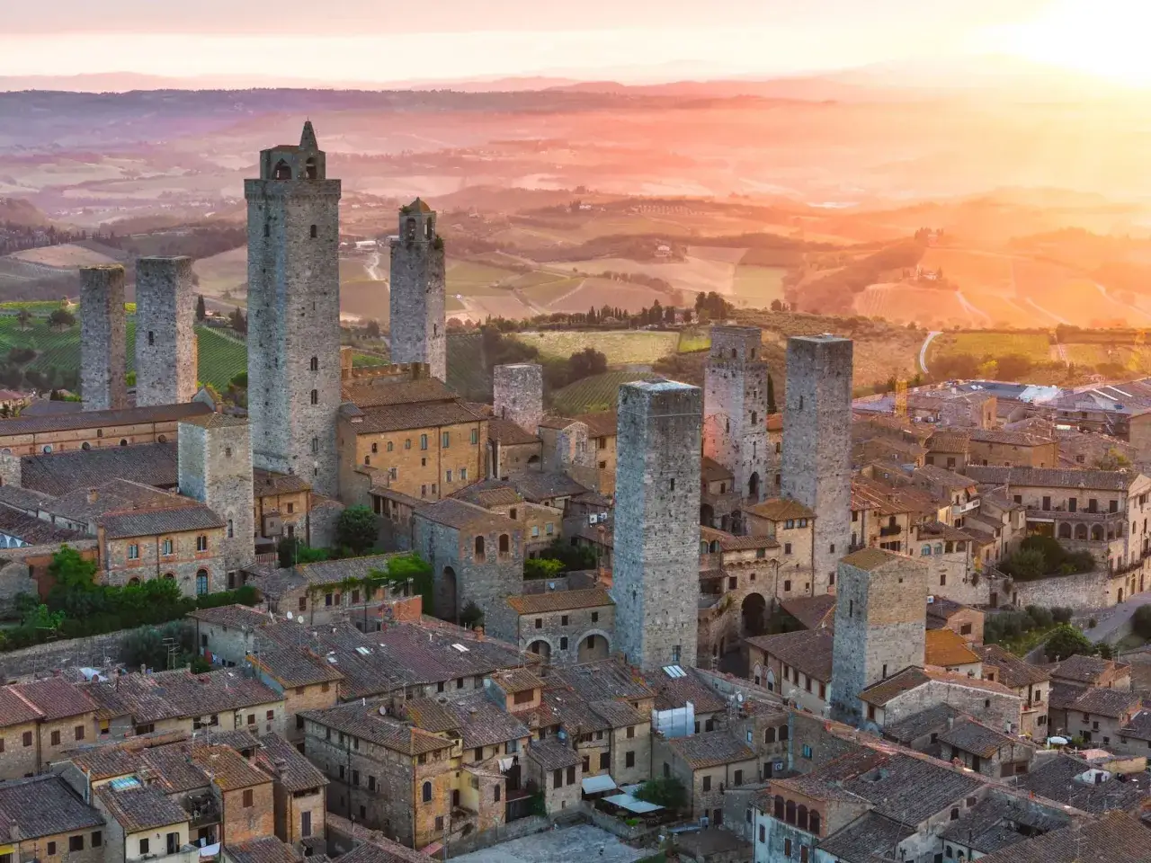 Torri medievali di San Gimignano si stagliano contro un tramonto dorato, con dolci colline toscane sullo sfondo.