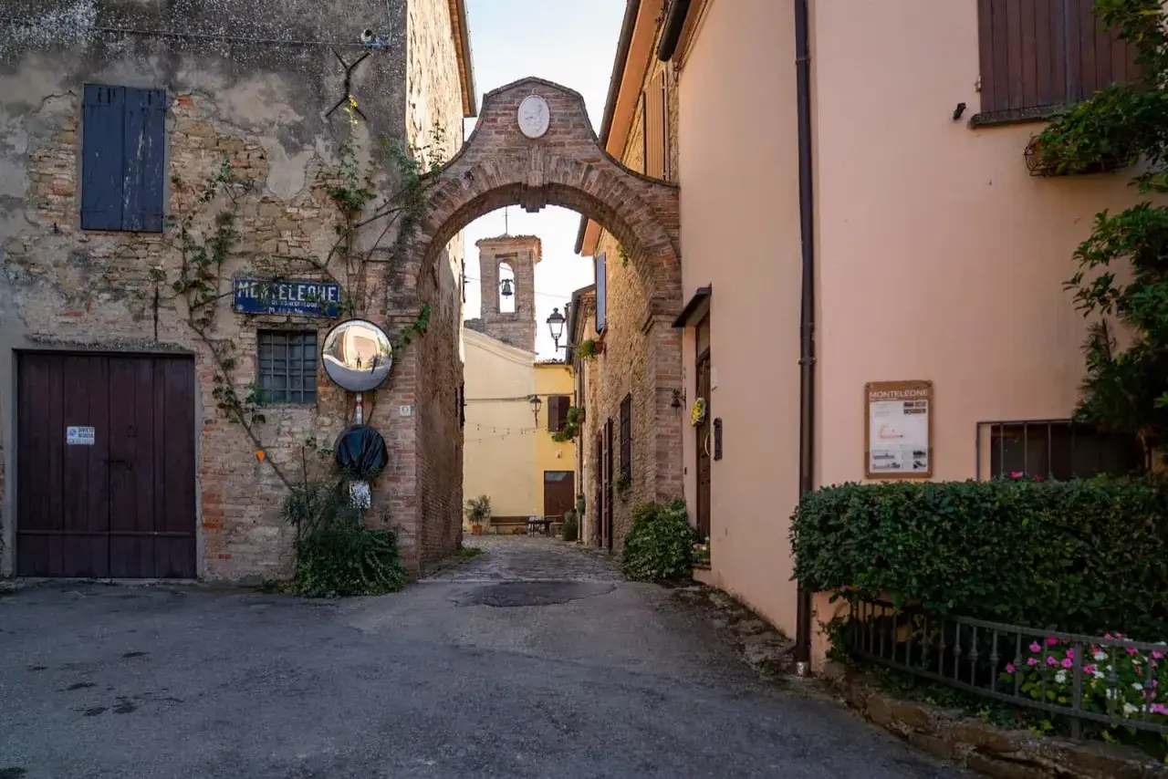 Un vicolo a Monteleone di Roncofreddo, con un arco in mattoni che conduce a una piazza con campanile.