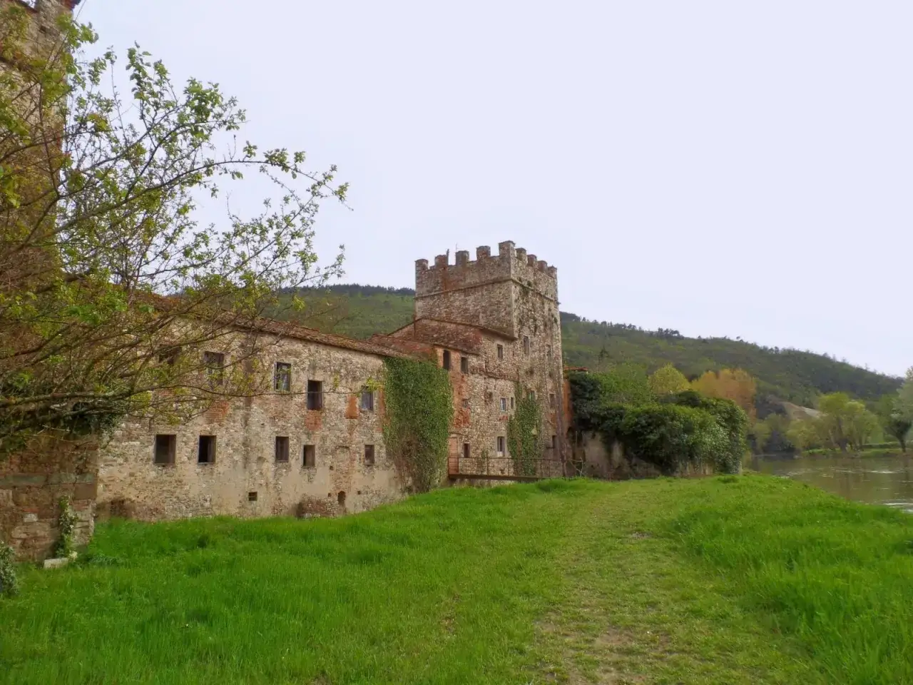 Antiche gualchiere di Remole, un borgo fortificato in pietra con torre merlata, immerso nel verde e affacciato su un fiume.