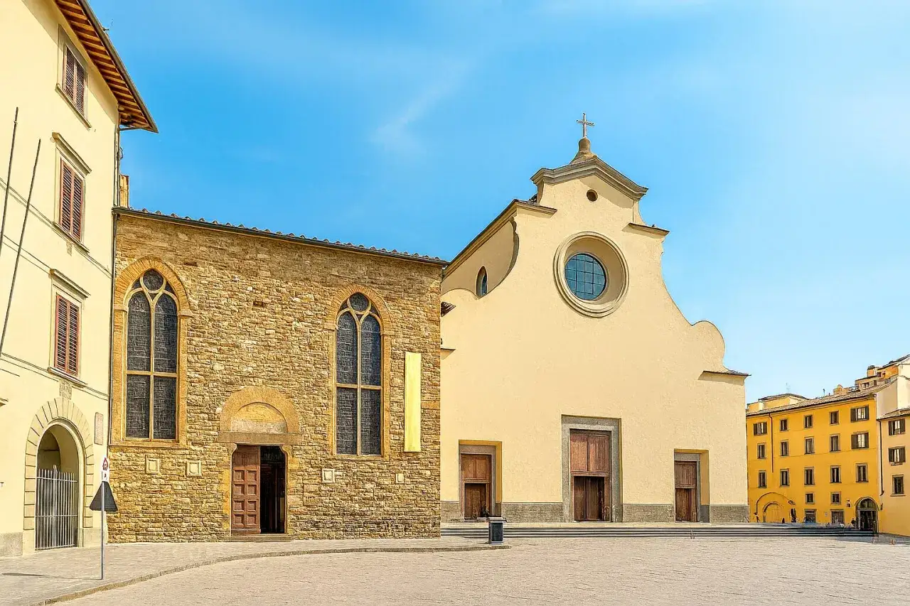 La piazza Santo Spirito a Firenze, con la sua chiesa in pietra e la facciata gialla, sotto un cielo azzurro.
