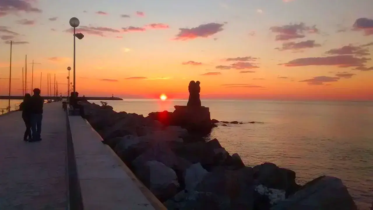 Tramonto sul mare, con una scultura di due amanti in primo piano. Un ricordo di una gita a Lucca e dintorni.