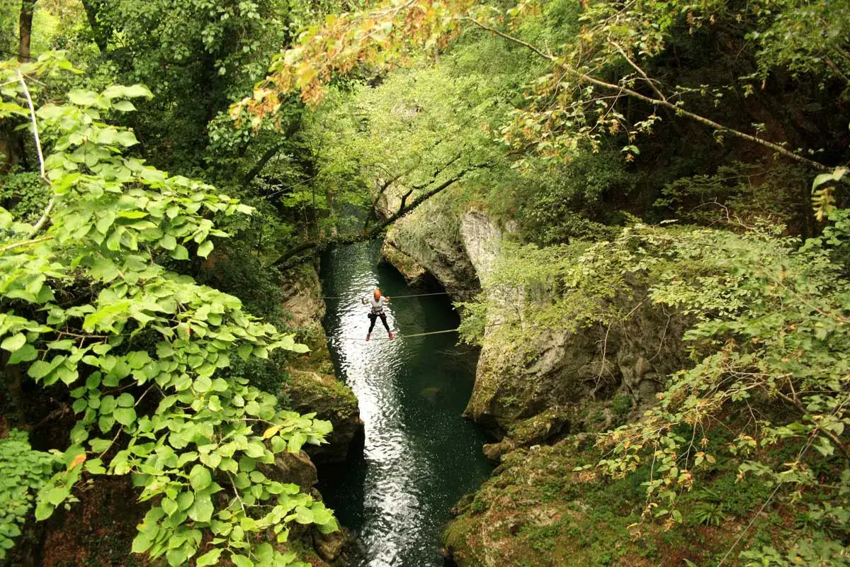 Persona cammina su un cavo teso sopra un fiume verde smeraldo, un'avventura nella laguna blu Bagni di Lucca.