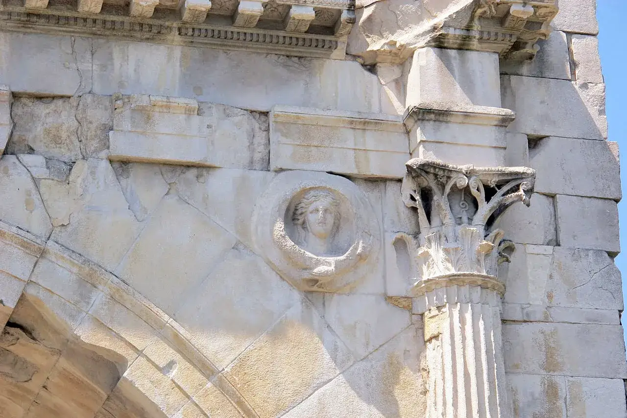 Dettaglio del volto scolpito nell'arco augusto di Rimini, con capitello corinzio e decorazioni in pietra.