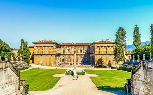Il maestoso Palazzo Pitti si staglia contro un cielo azzurro, circondato da giardini lussureggianti e antiche scalinate.