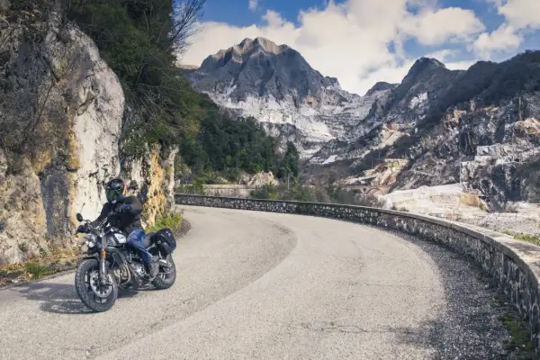 Motociclista su strada tortuosa con montagne di marmo sullo sfondo. Perfetto per itinerari moto Toscana 3 giorni.