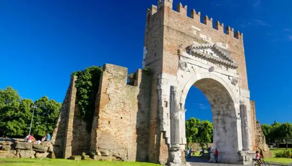L'imponente arco augusto rimini, con la sua antica pietra e la torre in mattoni, si staglia contro un cielo azzurro.