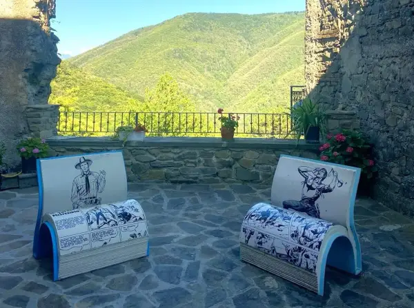 Due sedie a forma di libro con fumetti western, in un cortile con vista sulle colline verdi. Montereggio, paese dei librai, offre un angolo lettura unico.
