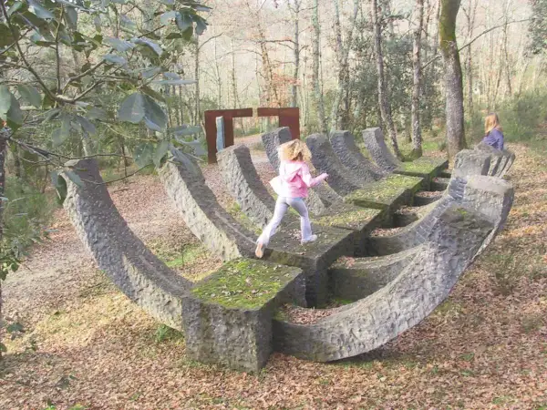 Bambini esplorano un **museo a cielo aperto in Toscana**, tra sculture in pietra e alberi secolari.