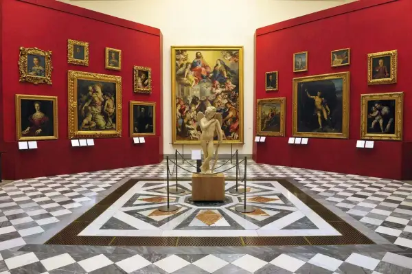 Sala con opere d'arte nei musei d'arte a Firenze. Statua di Cupido al centro, circondata da dipinti su pareti rosse.