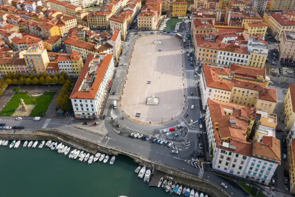 Vista aerea della piazza della Repubblica a Livorno, con edifici storici, un monumento centrale e barche ormeggiate nel canale.