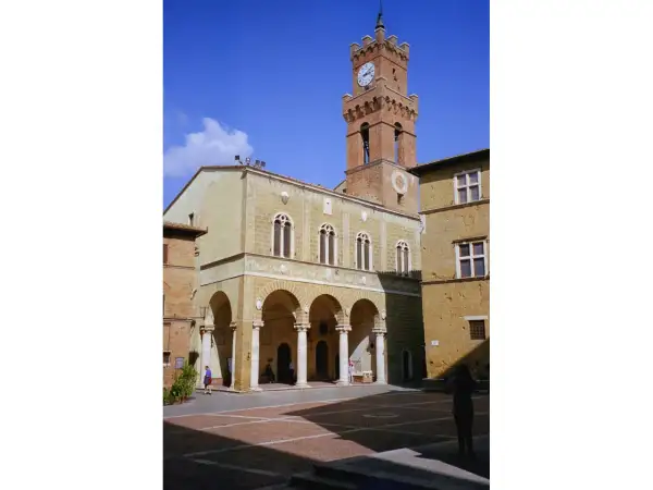 Il **Palazzo Comunale di Pienza** domina la piazza con la sua torre dell'orologio. Archi eleganti e finestre gotiche caratterizzano l'edificio.