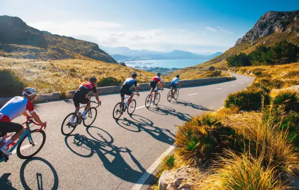 Ciclisti su strada panoramica, ideali per itinerari bici 3 giorni. Paesaggio montuoso e mare sullo sfondo.