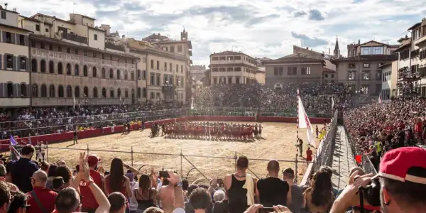 Un campo di sabbia a Firenze, gremito di spettatori, ospita un'intensa partita di calcio storico.