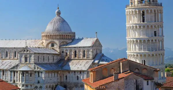 Pisa cosa vedere: il Duomo e la Torre Pendente, capolavori romanici che svettano nel cielo azzurro, con le montagne sullo sfondo.
