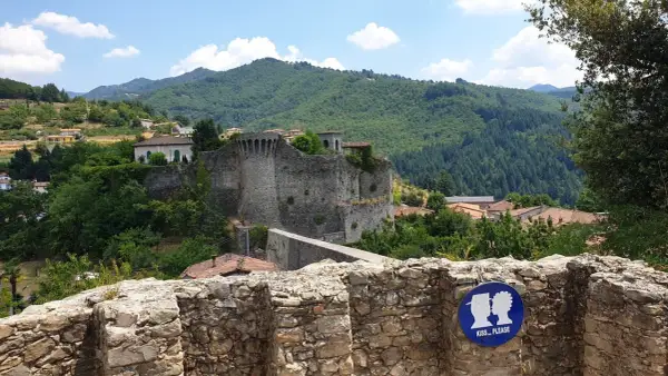 La rocca di Castiglione domina un borgo tra colline verdi. Un cartello invita a baciarsi.