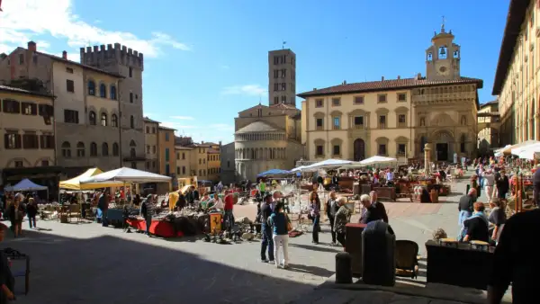 Piazza gremita per l'Arezzo antique market, tra bancarelle di antiquariato e palazzi storici sotto un cielo azzurro.