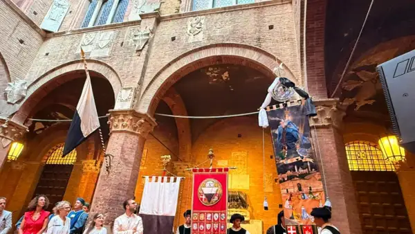 Sfilata storica a Siena con stendardi e costumi d'epoca, evocando l'atmosfera del Palio.