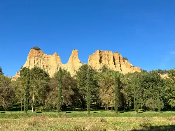Le maestose balze del Valdarno si stagliano contro un cielo azzurro, circondate da una rigogliosa vegetazione e cipressi slanciati.
