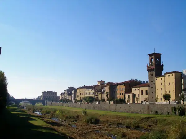 Pescia: cosa vedere? Un fiume serpeggia tra edifici storici e una torre imponente, sotto un cielo azzurro.