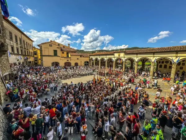 Folla in piazza per il palio dei rioni Castiglion Fiorentino, con figuranti in costume e bandiere.