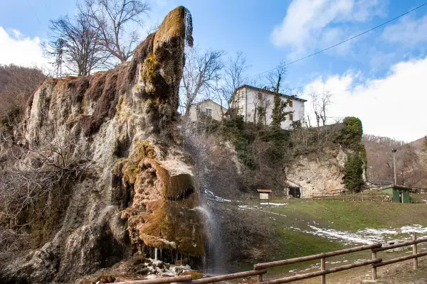 Cascata calcarea presso le grotte di Labante, con case in collina e cielo azzurro.