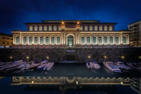 Il mercato di Livorno illuminato di notte, con barche ormeggiate e il loro riflesso sull'acqua.