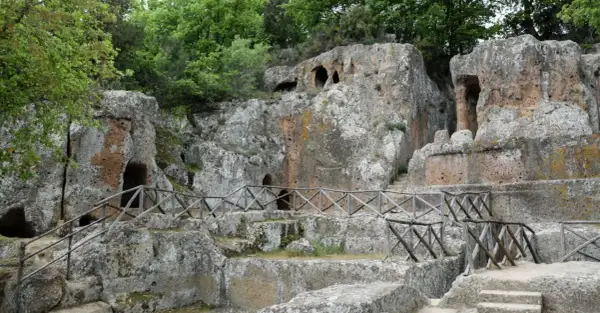 Antiche tombe scavate nella roccia, parte di siti etruschi, con sentieri e recinzioni in legno.