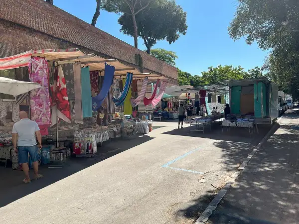 Mercato all'aperto a Grosseto, con bancarelle colorate di tessuti e abbigliamento sotto un cielo azzurro.