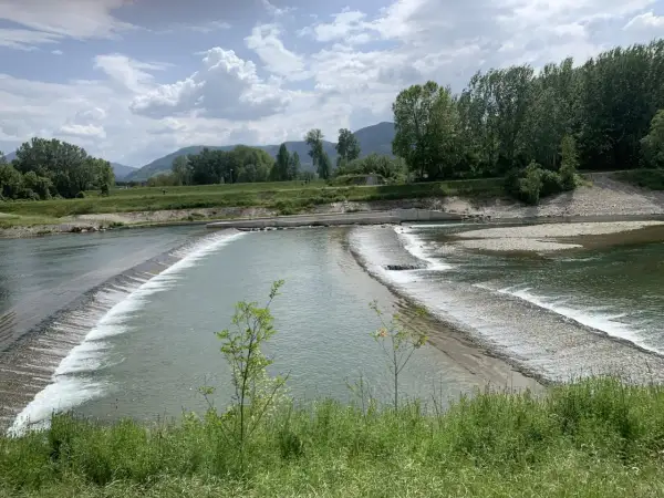 Il **parco fluviale del Serchio** offre uno spettacolo di acqua che scorre su dighe naturali, circondato da verdi colline e alberi rigogliosi sotto un cielo nuvoloso.