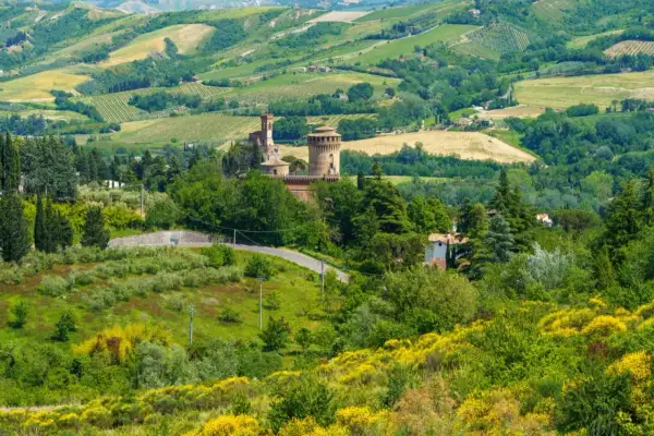 Colline verdi con un castello medievale e campi coltivati, tipiche delle strade panoramiche in Emilia Romagna.