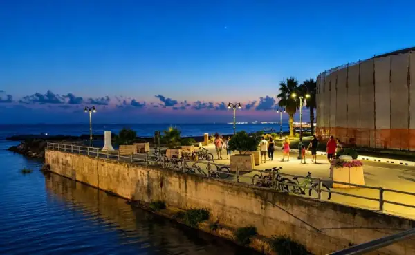 Passeggiata serale lungo il mare a Follonica, con persone che camminano e biciclette parcheggiate.